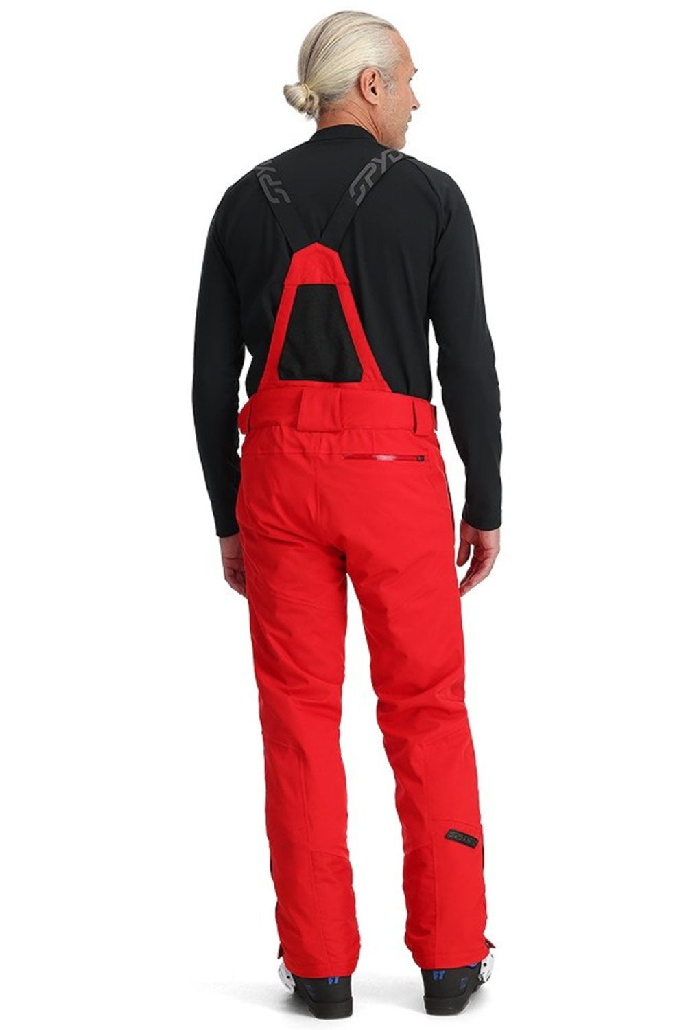 Person wearing a black jacket and red bib overalls on a white background