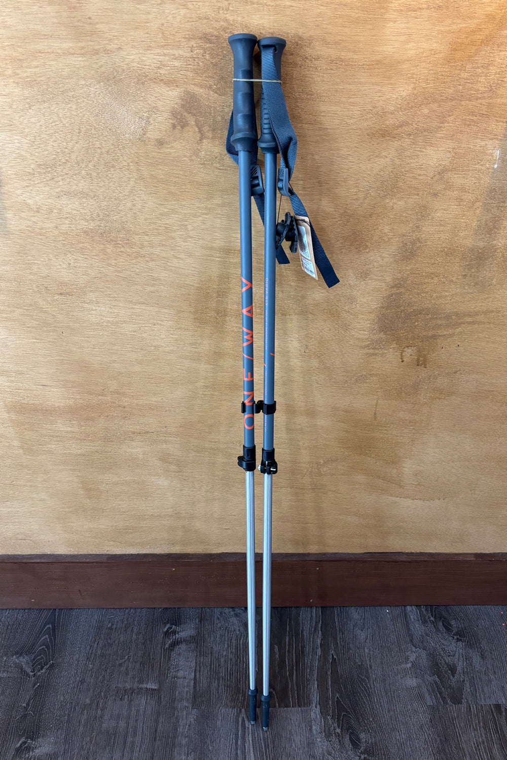 Two gray adjustable skiing poles with black grips on a wooden floor.