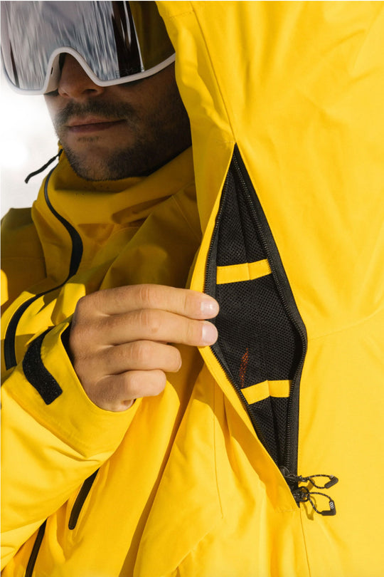 Person wearing a yellow jacket with a black zipper detail, with a neutral background.