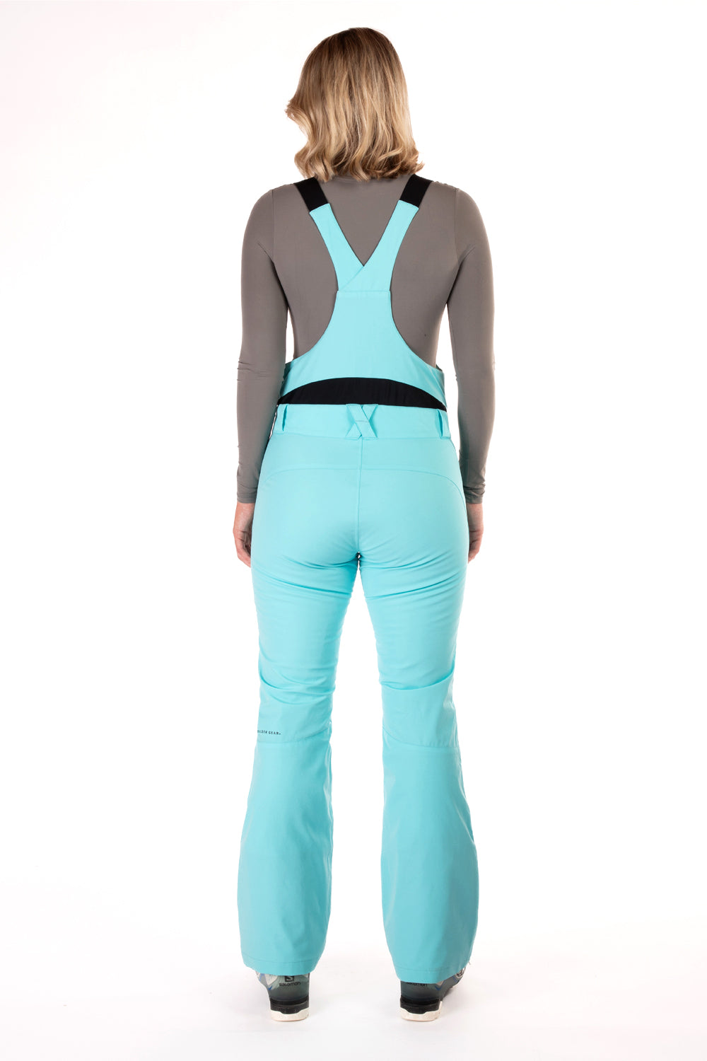 Person wearing turquoise snow pants with black straps on a white background