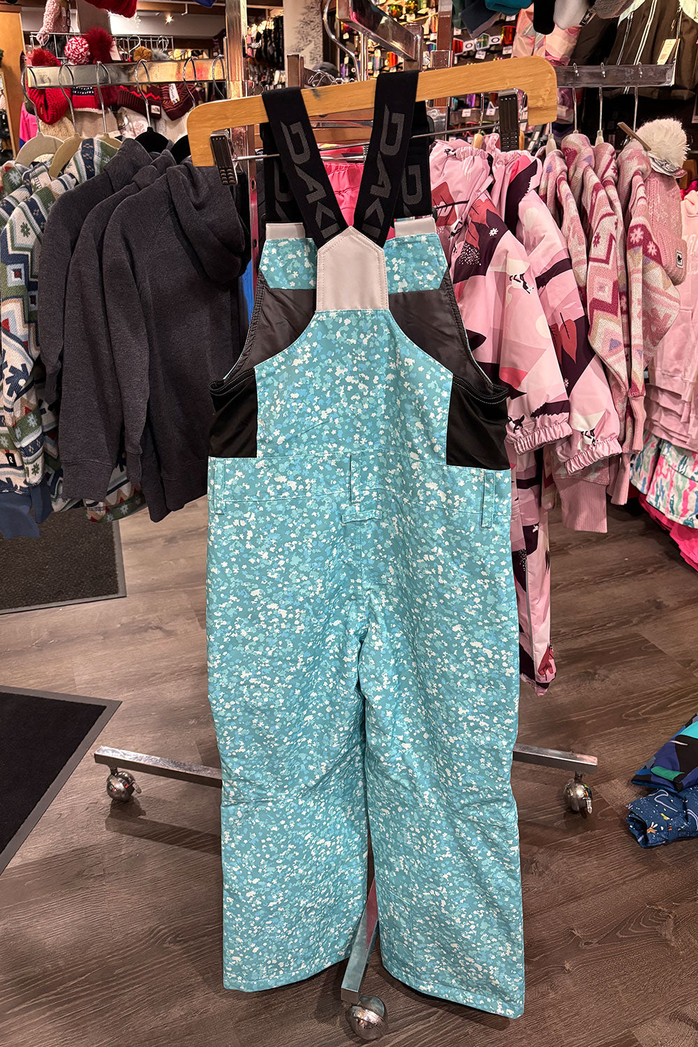 Turquoise snow pants with floral pattern on a rack in a store setting