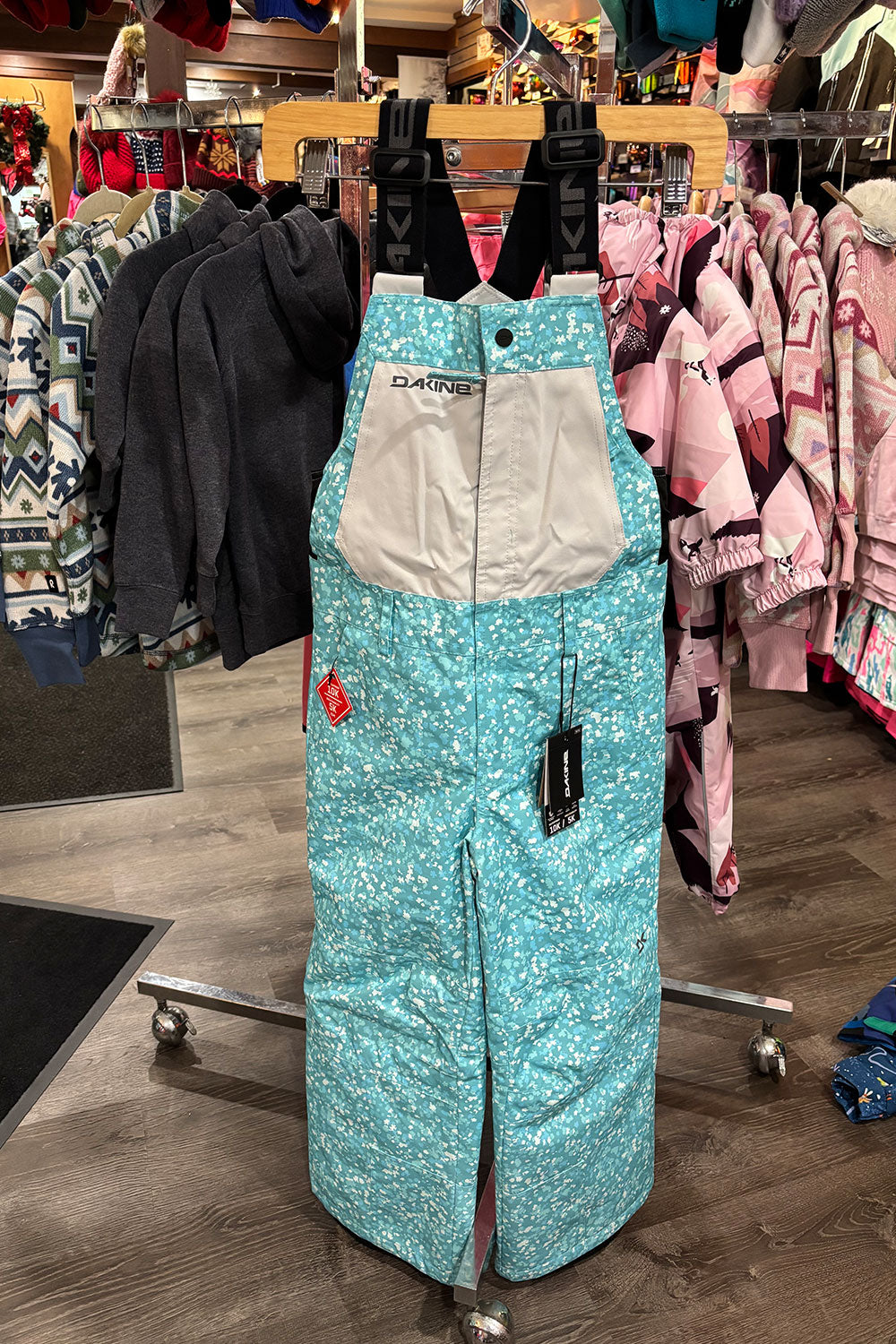 Turquoise snow pants with gray lining on a hanger in a store setting