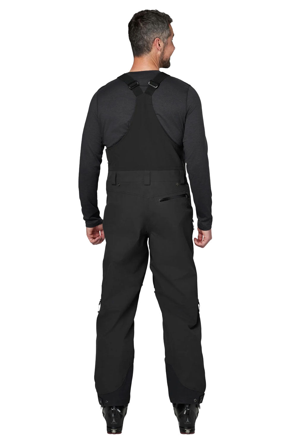 Person wearing black ski bibs with suspenders on a white background