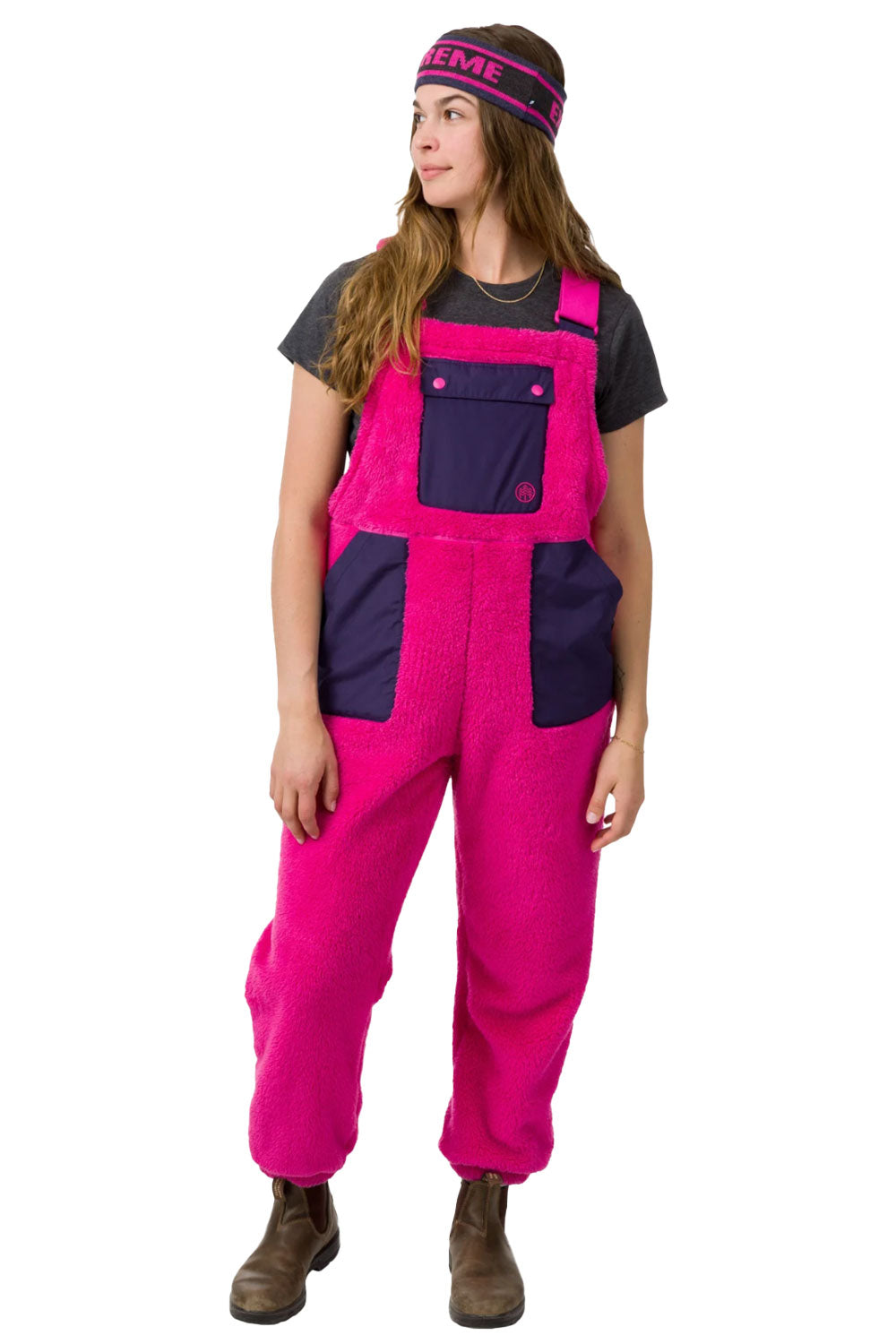Person wearing bright pink and navy blue bib overalls on a white background