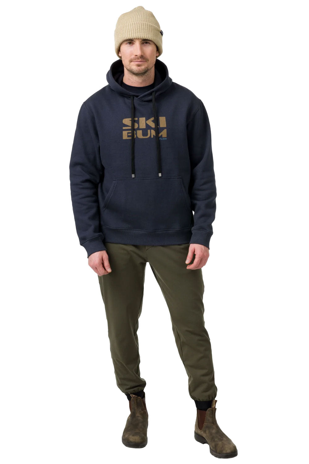 Man wearing a navy hoodie with 'Ski Bum' text, beige beanie, and green pants on a white background