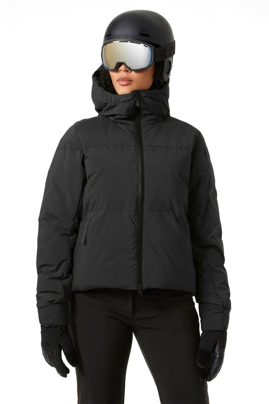 Person wearing a black puffy ski jacket, helmet, goggles, and gloves on a white background