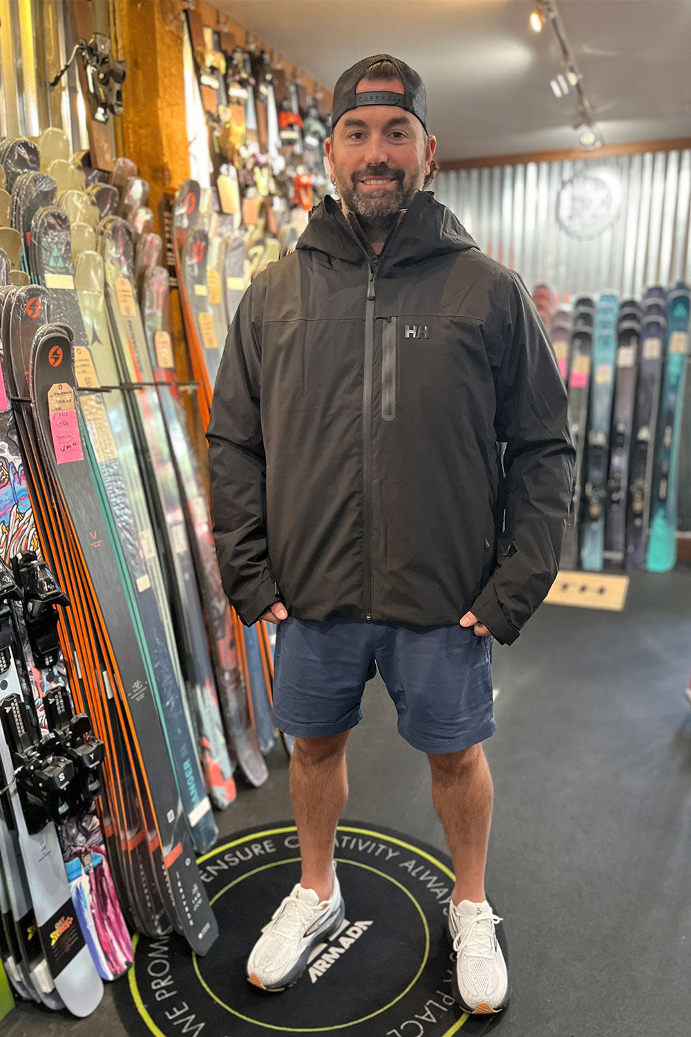 Man wearing a black jacket standing in a ski shop with skis on display.