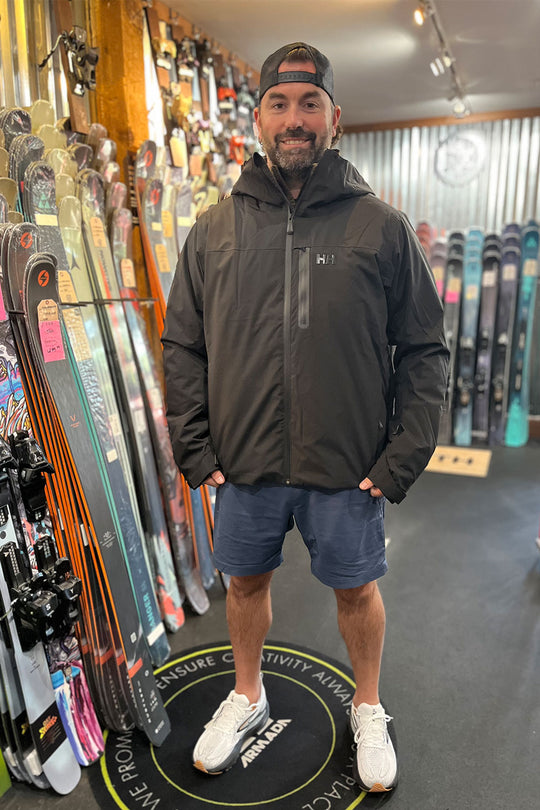 Man wearing a black jacket standing in a ski shop with skis on display.