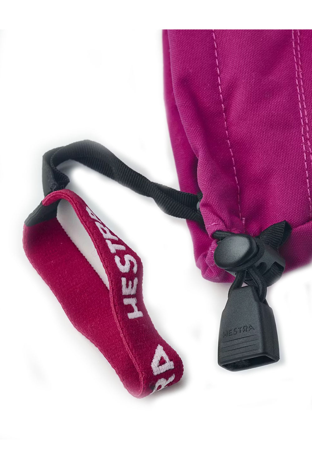 Close-up of a pink mitten with a black strap and Hestra logo on a white background