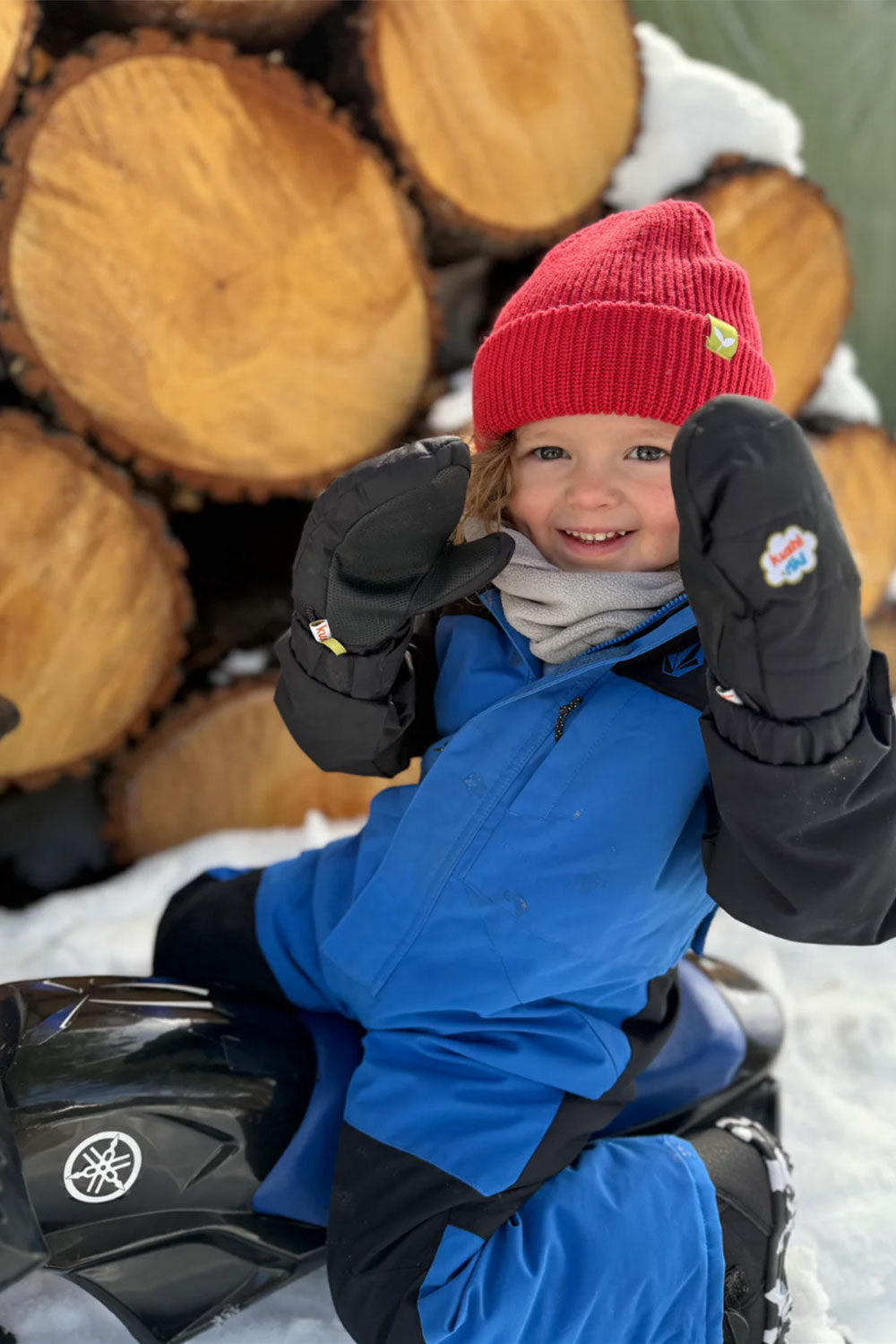 Child in winter clothing sitting in front of stacked logs