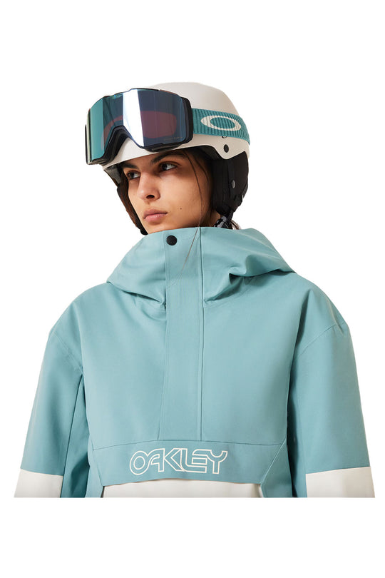 Person wearing a teal jacket with Oakley branding and a helmet with goggles on a white background