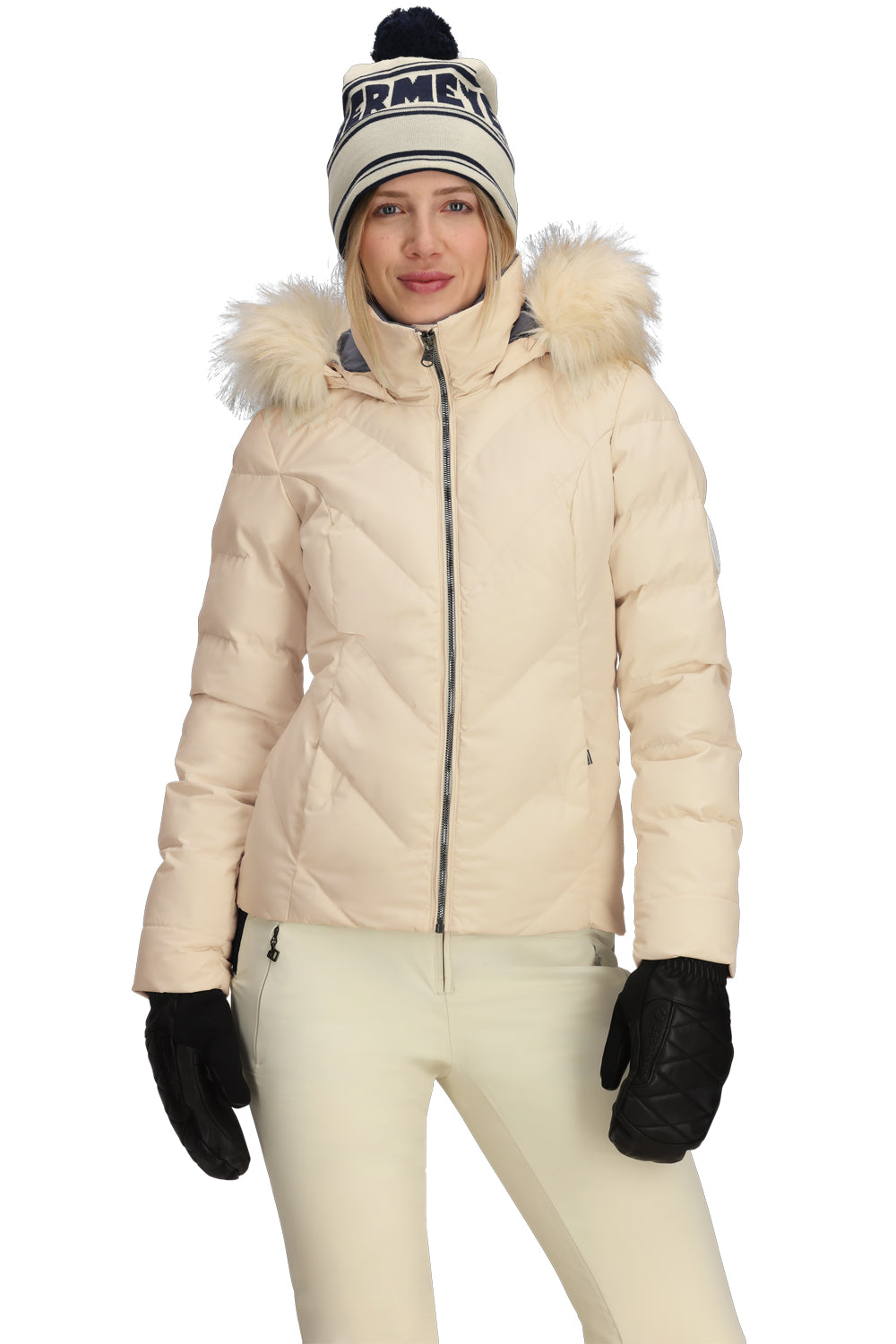 Person wearing a beige winter coat with fur hood, white pants, black gloves