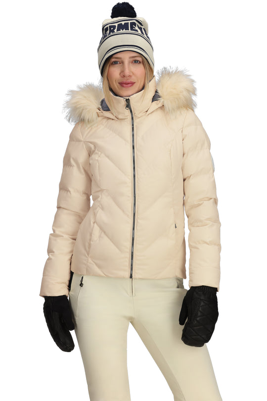 Person wearing a beige winter coat with fur hood, white pants, black gloves