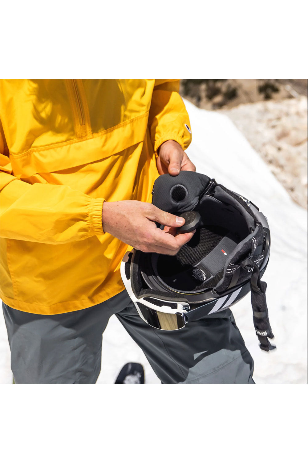 Person in yellow raincoat holding a black helmet on a snowy path