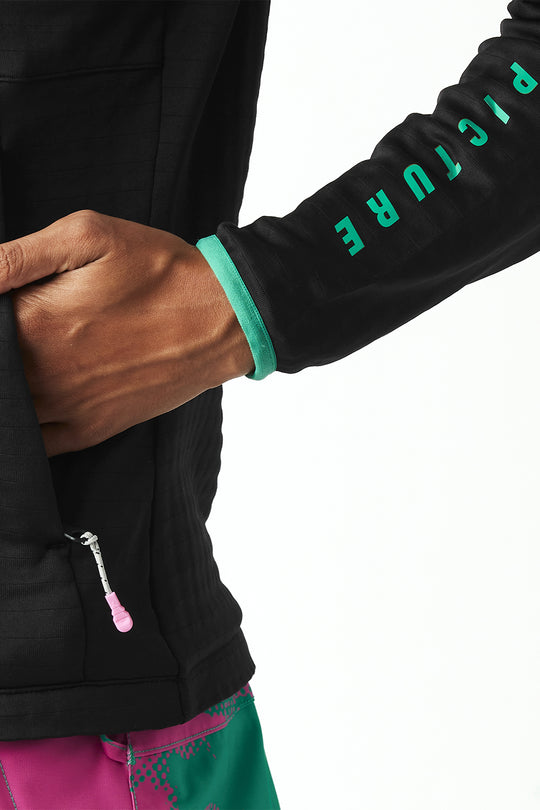 Close-up of a black jacket with green text on the sleeve, worn by a person.