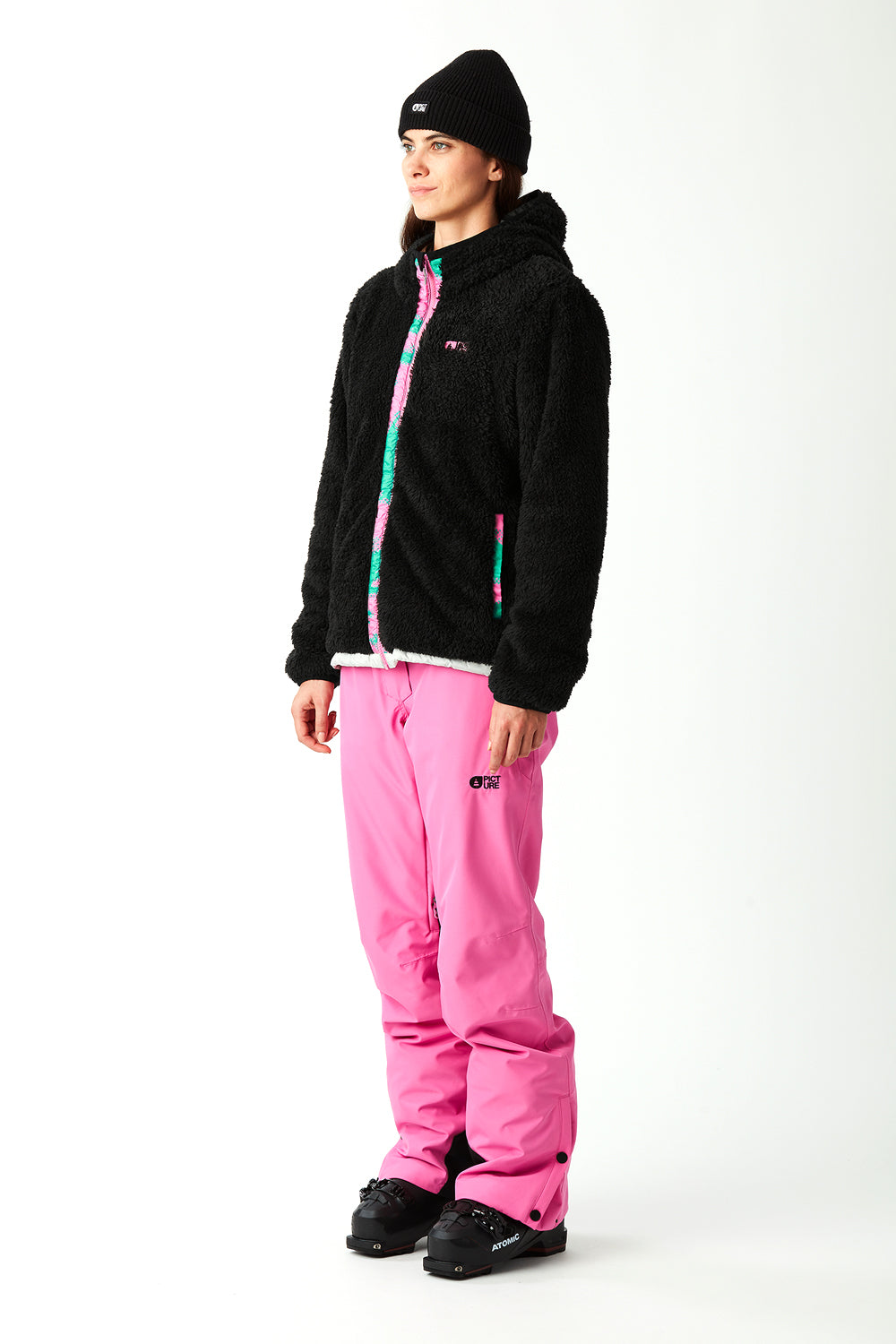 Person wearing a black jacket with colorful accents and pink snow pants on a white background