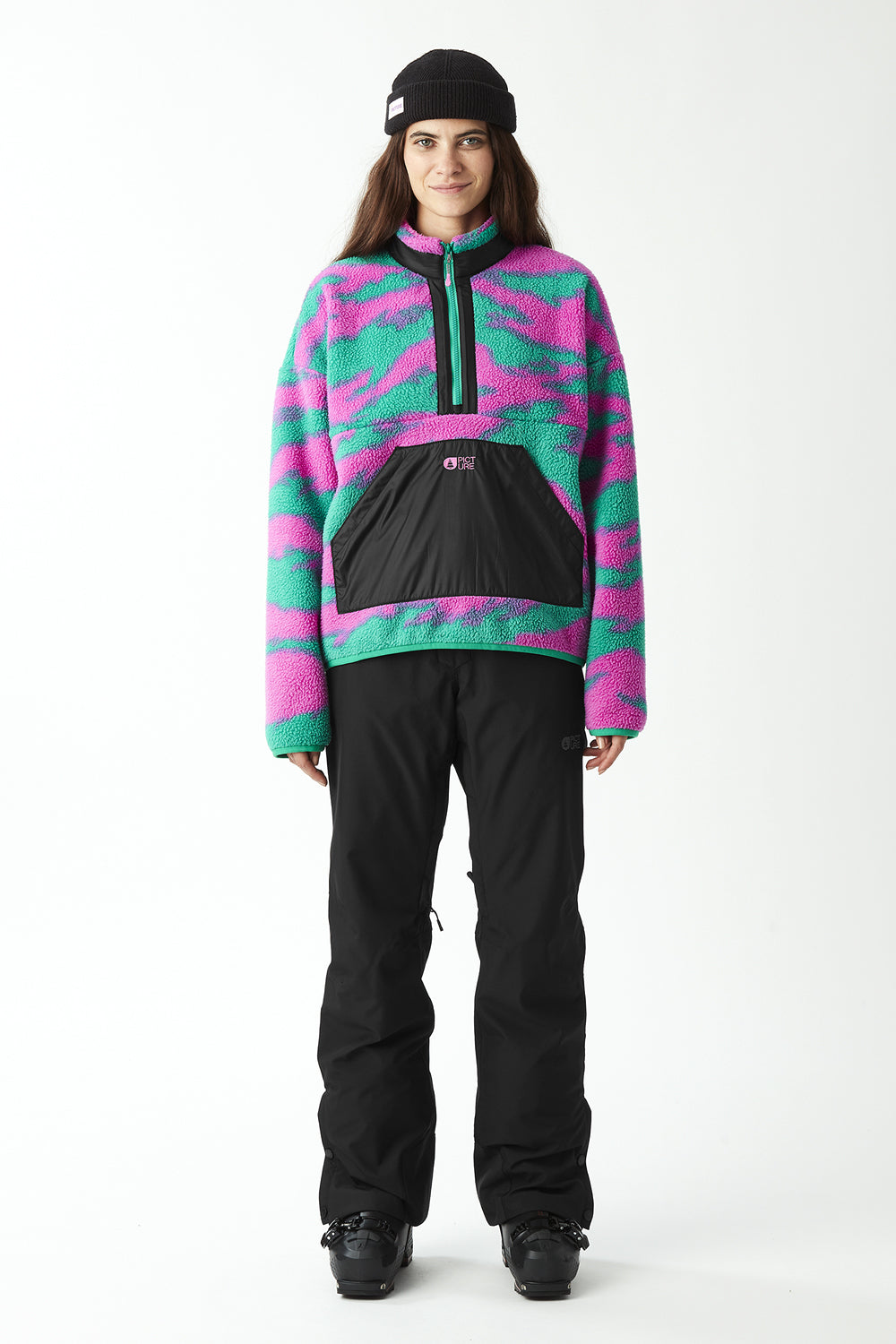 Person wearing a colorful fleece jacket and black pants on a white background