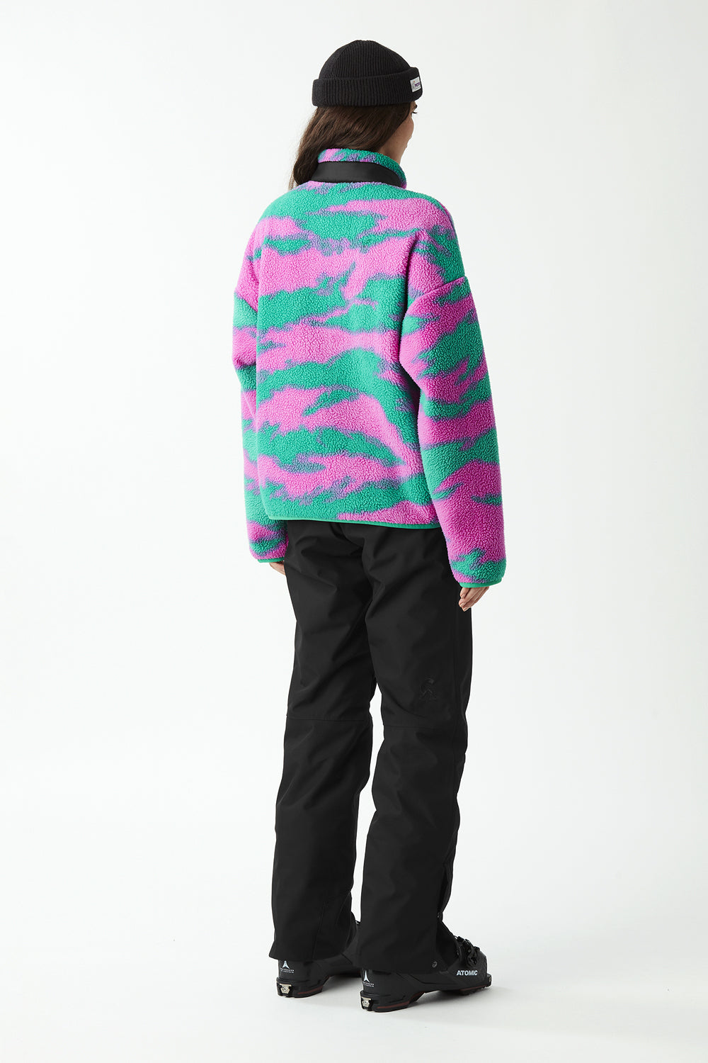 Person wearing a colorful camouflage fleece jacket and black pants on a white background