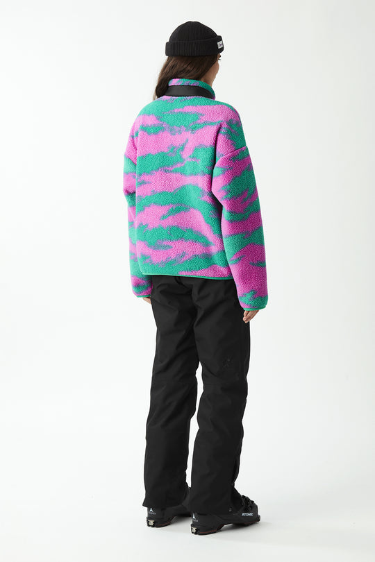 Person wearing a colorful camouflage fleece jacket and black pants on a white background