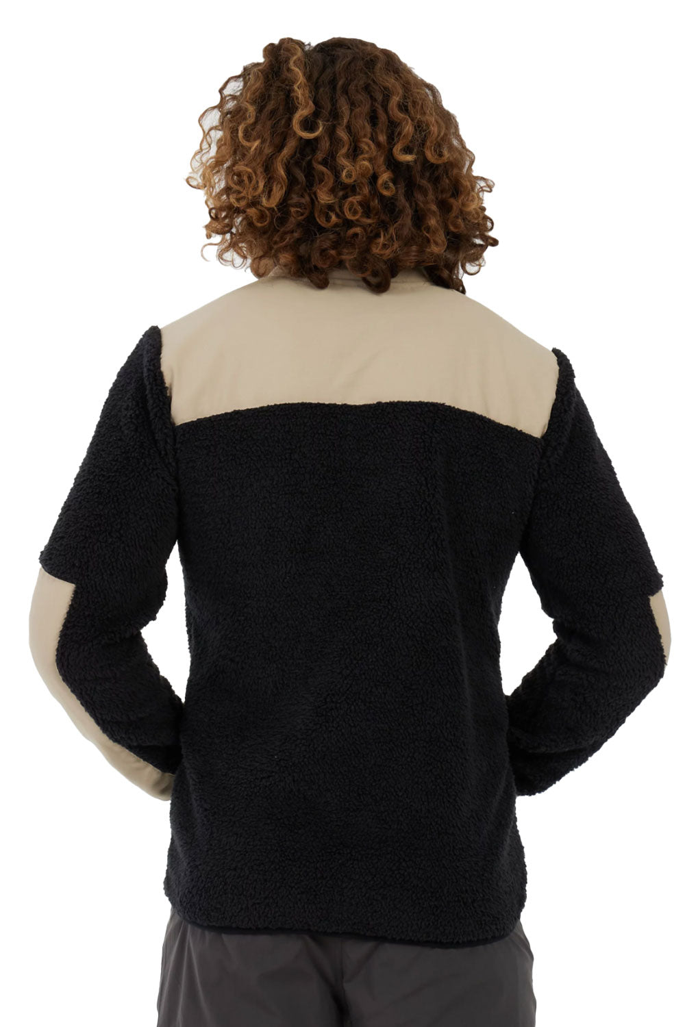 Person wearing a black and beige sweater with hands in pockets on a white background