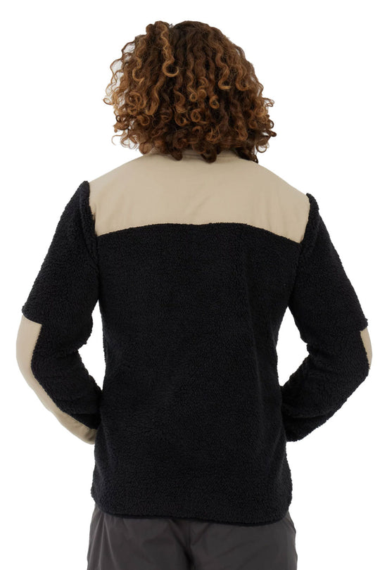 Person wearing a black and beige sweater with hands in pockets on a white background