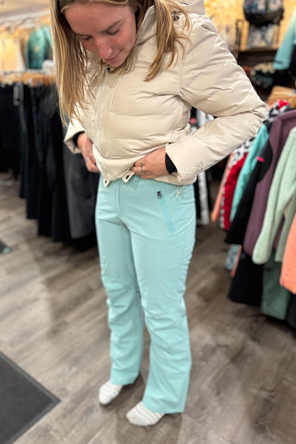 Person wearing a beige puffer jacket and light blue pants in a clothing store.
