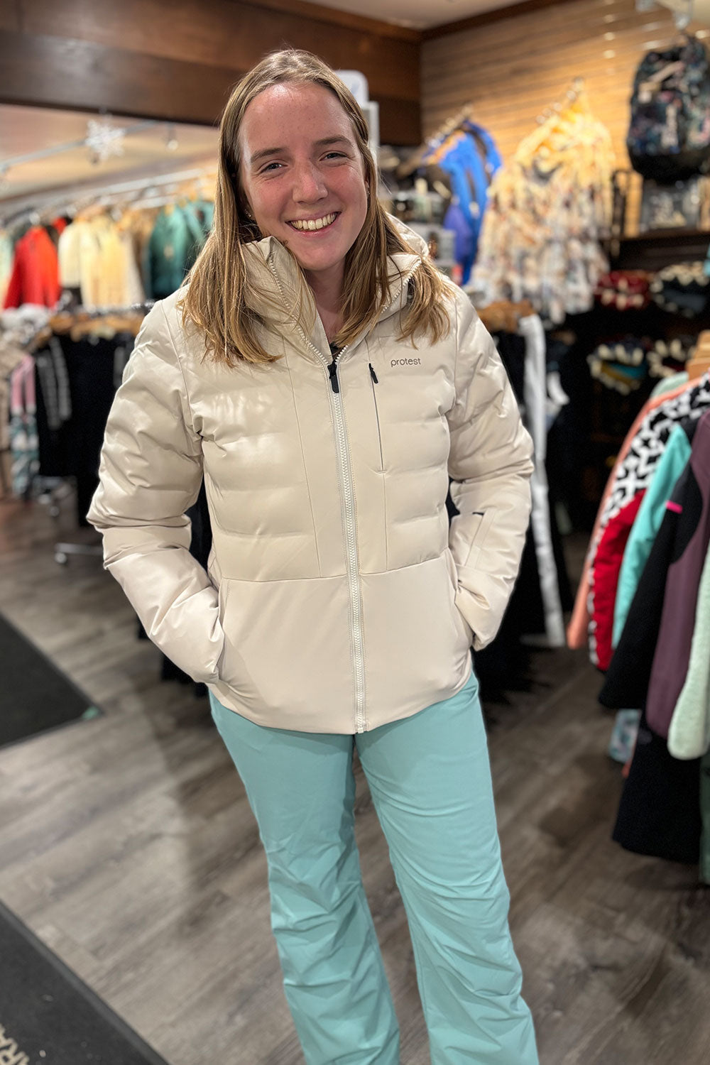 Woman wearing a beige puffer jacket and light blue pants in a store setting.