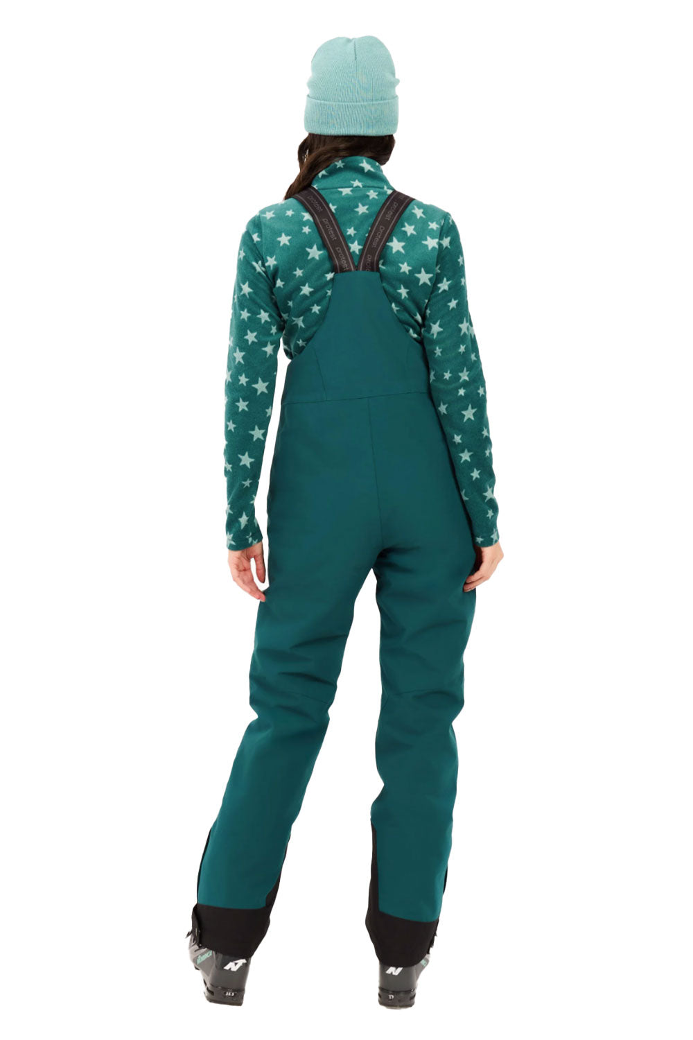 Person wearing a green star-patterned top and teal bib overalls on a white background