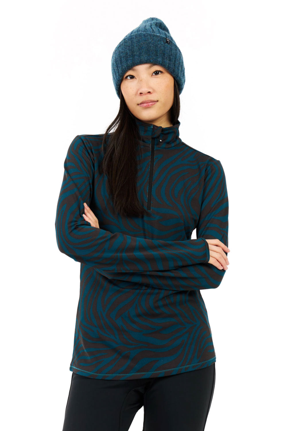 Woman wearing a teal and black patterned pullover with a matching beanie on a white background