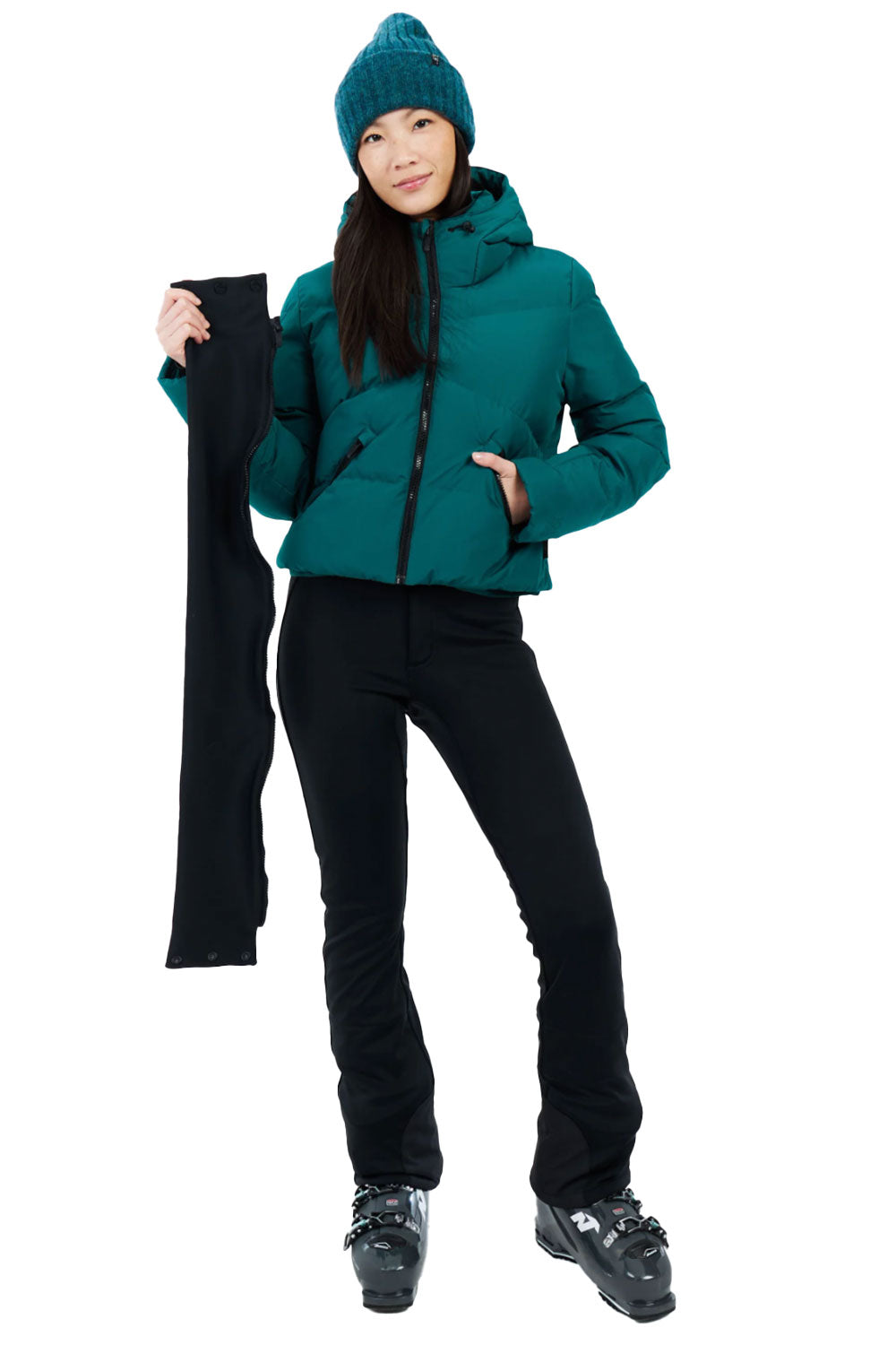 Person wearing a teal jacket and black pants holding a black ski pole on a white background