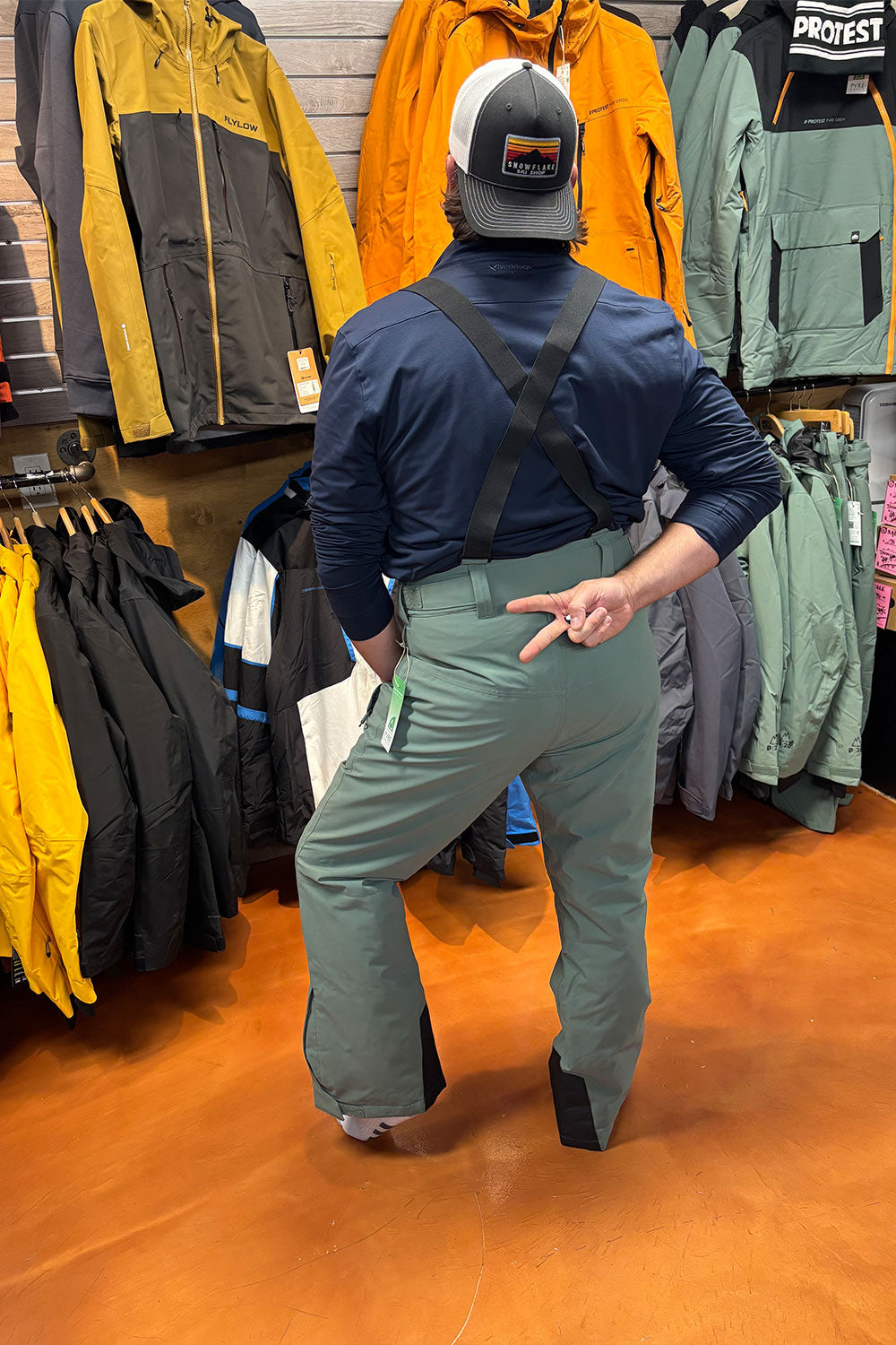 Person wearing a blue jacket and green pants in a store with jackets on display.