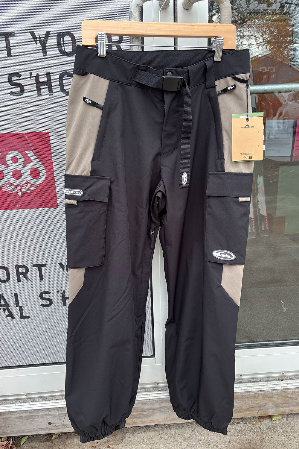 Black and beige pants on a hanger with a store window in the background