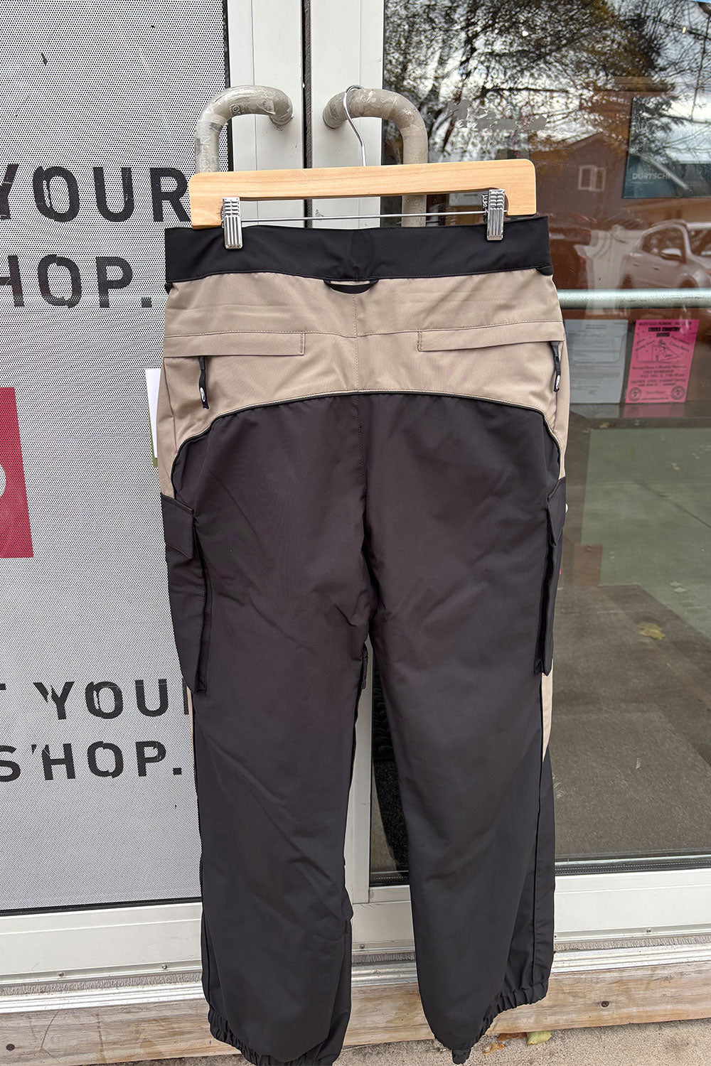 Black and beige pants on a hanger against a glass door background