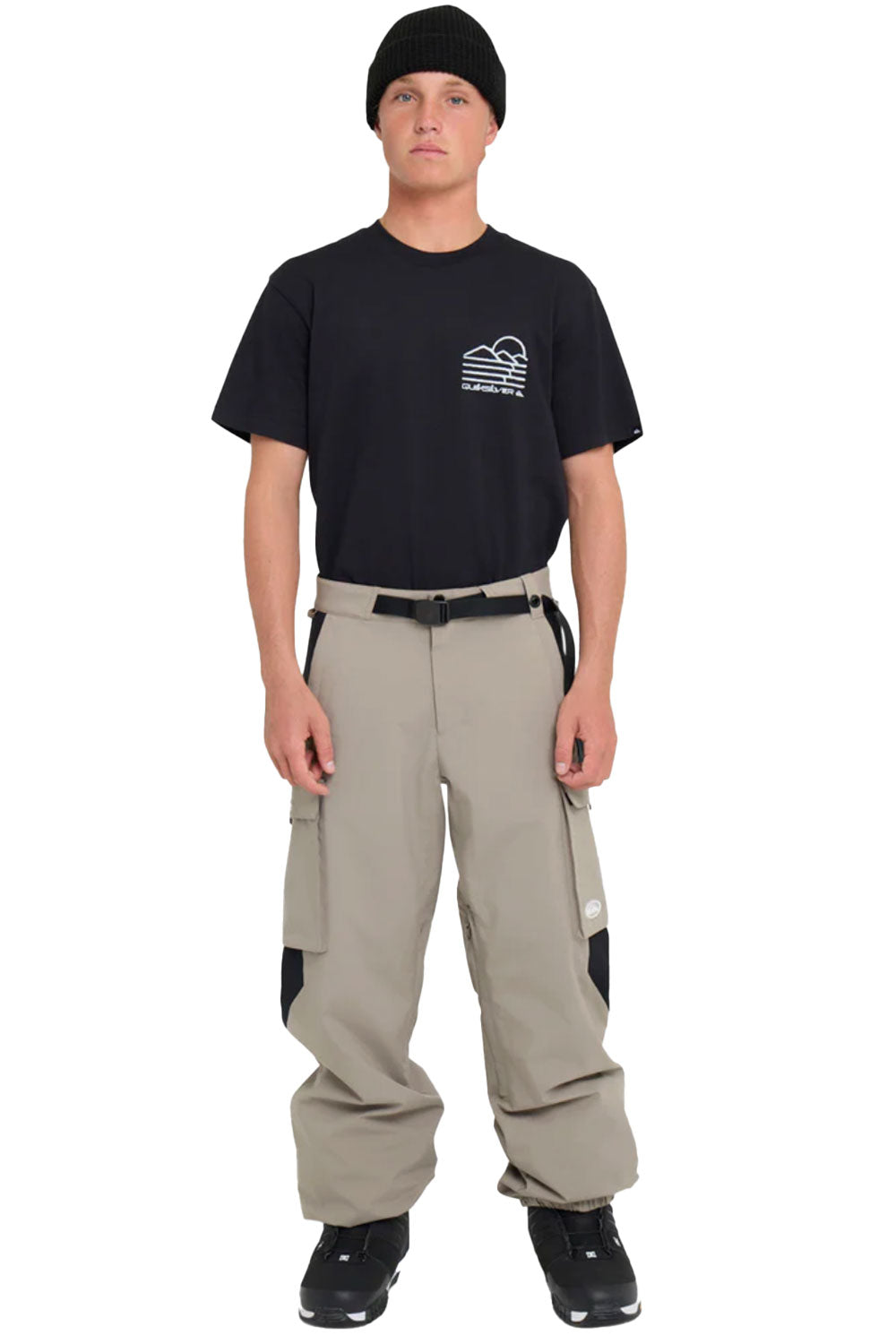 Person wearing a black t-shirt with a logo and beige pants on a white background