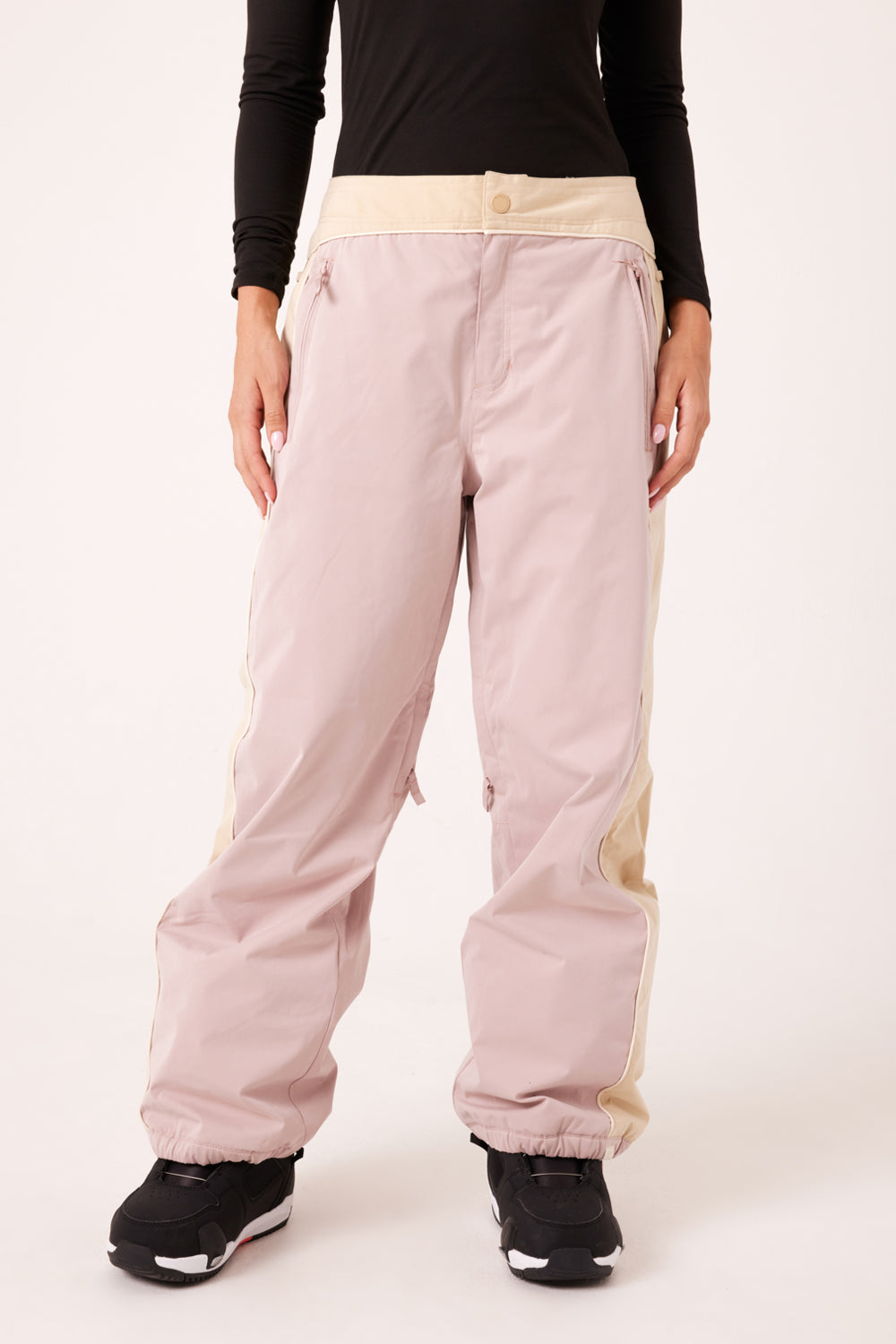 Light pink snowboard pants with beige accents worn by a person on a white background