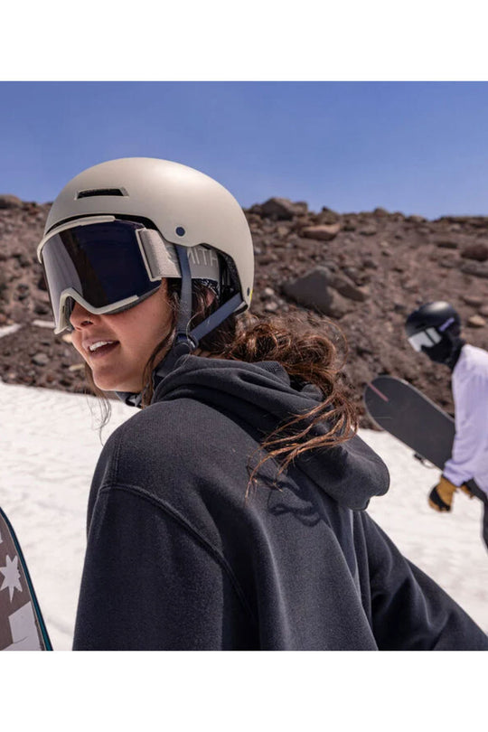 Person wearing a helmet and goggles on a snowy mountain with another person in the background.