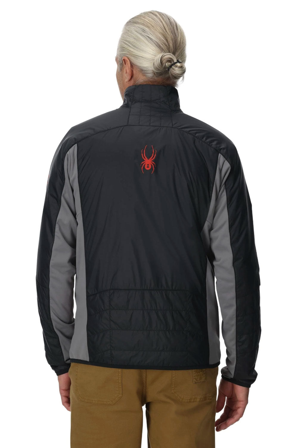 Person wearing a black and gray jacket with a red logo on the back, standing against a white background.