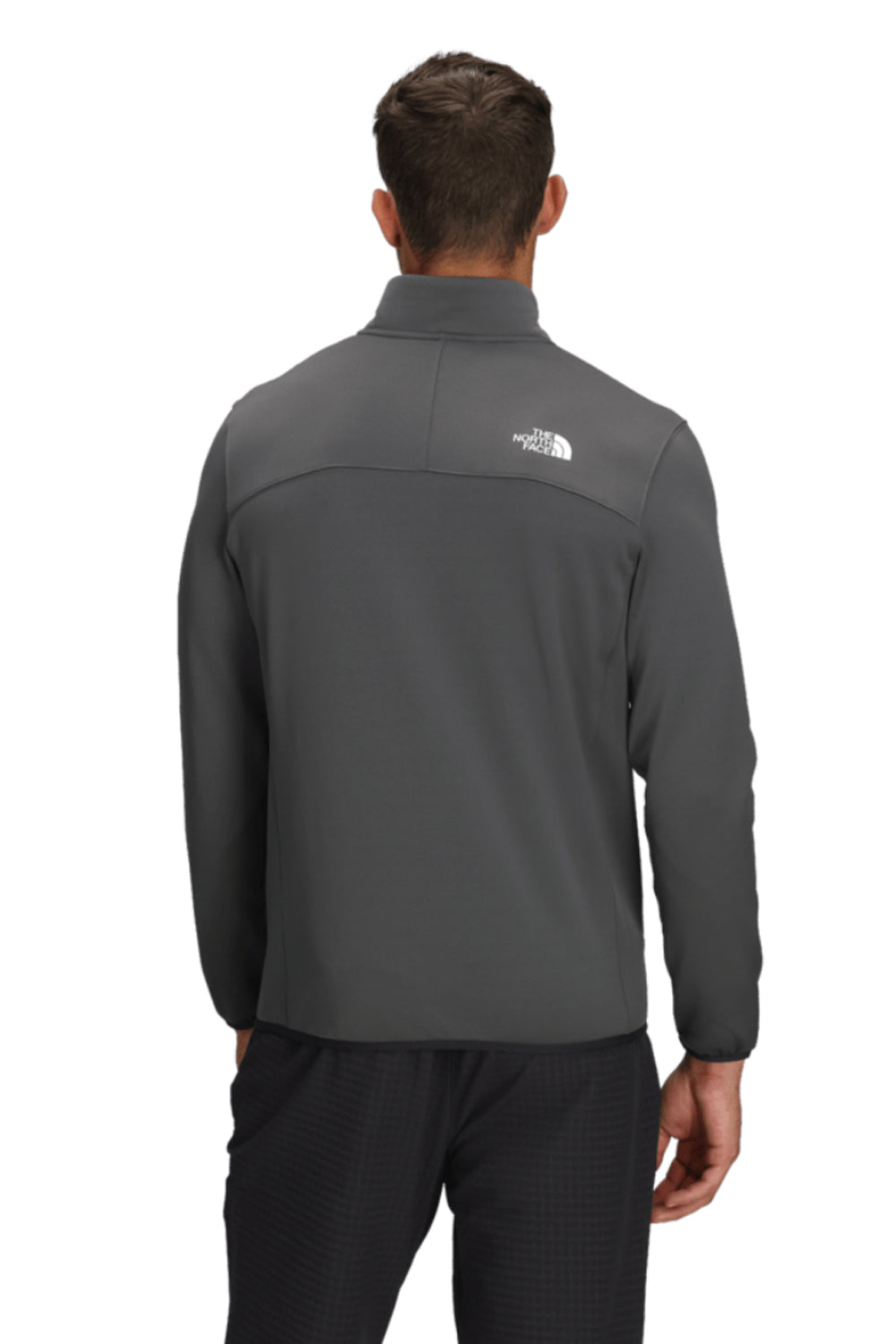 Person wearing a gray jacket with a brand logo on the back, standing against a white background