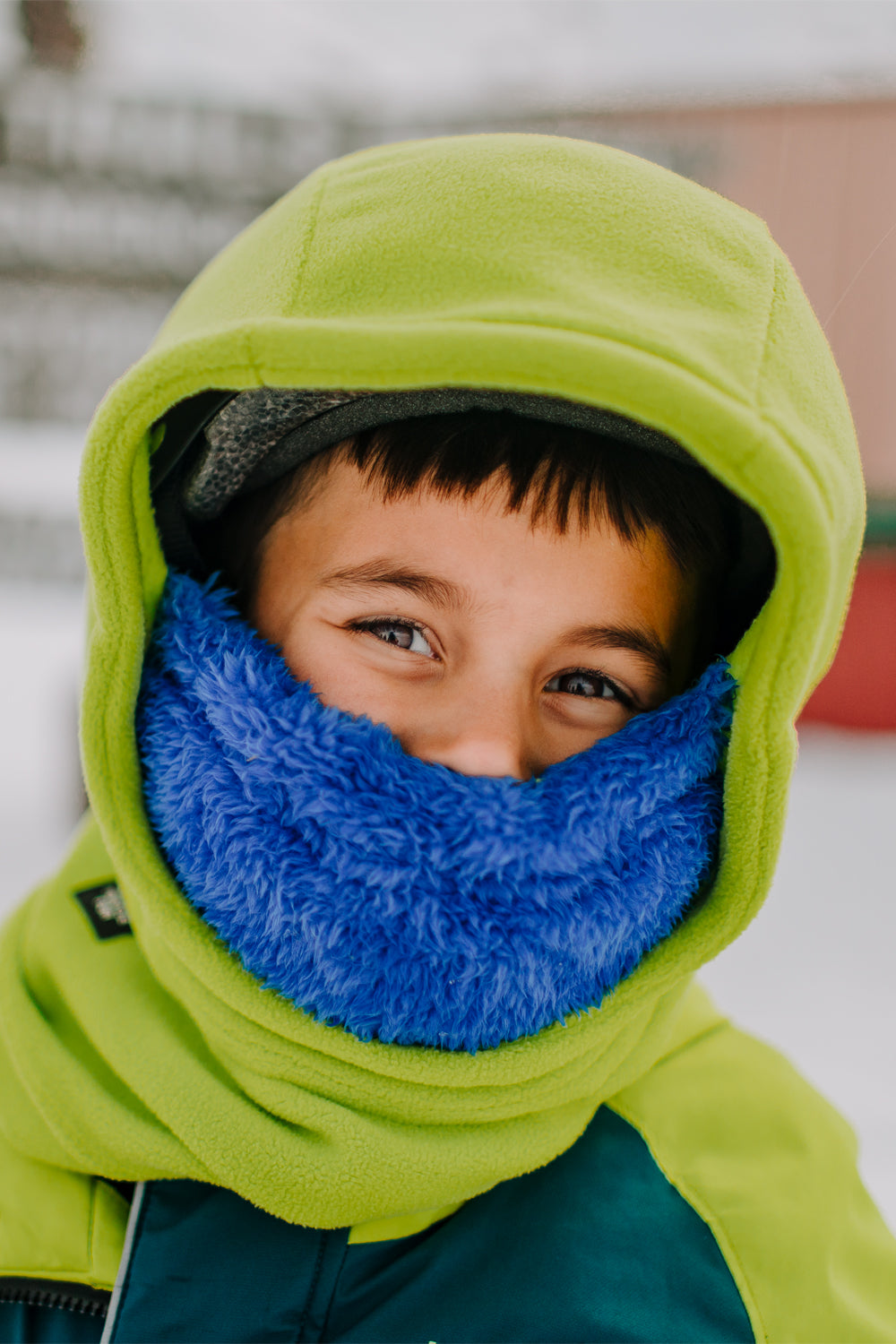 Child wearing a green & blue balaclava in a snowy outdoor setting