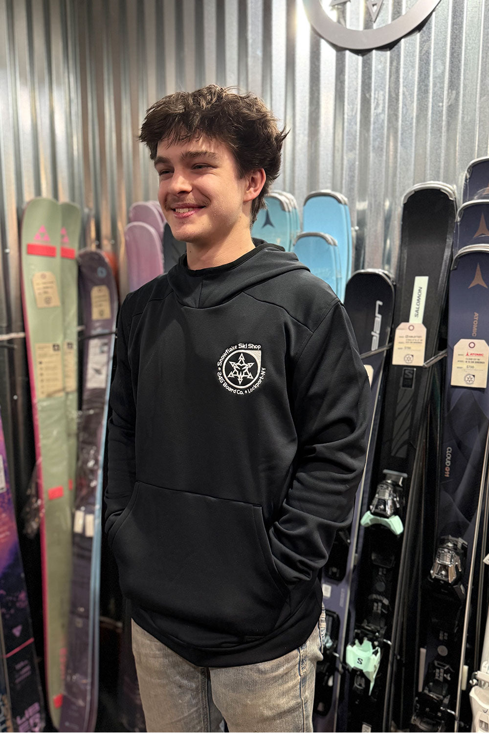 Person wearing a black hoodie with a logo in front of skis