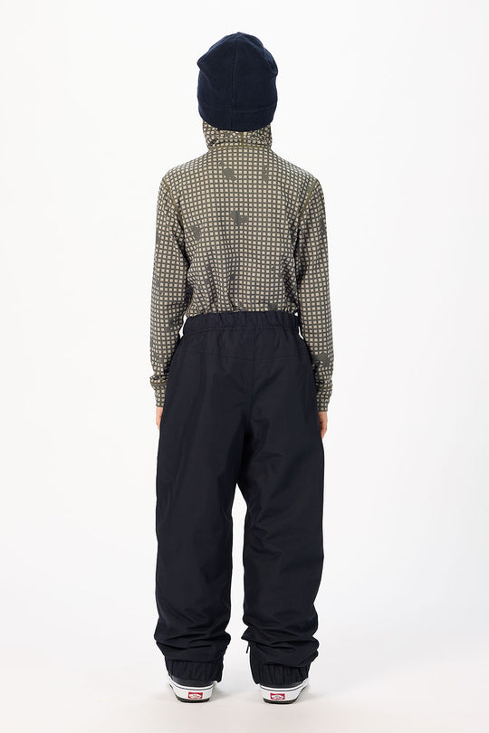 A person shown from the back wearing a dark navy beanie, a long-sleeve high-neck patterned shirt in olive and white, loose black pants, and white sneakers, against a plain white studio background.