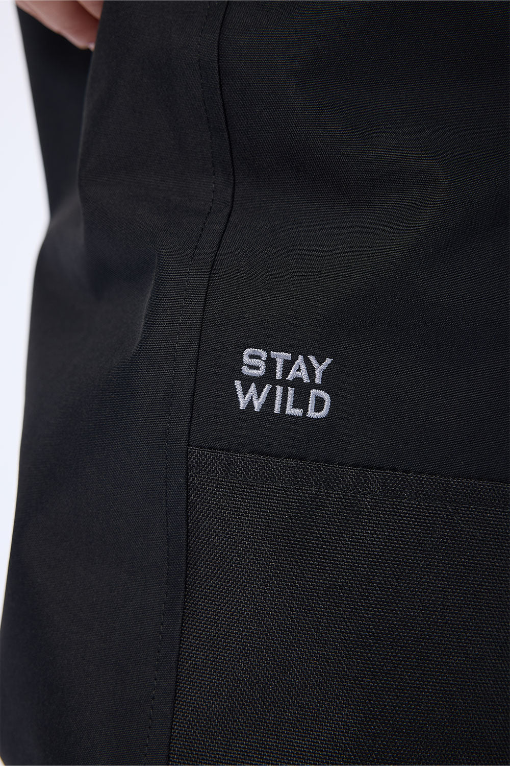Close-up of a black garment with a small white embroidered logo reading 'STAY WILD' on the chest.