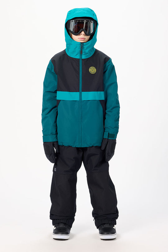 A child wearing a teal and black ski jacket with matching black snow pants, black gloves, and ski goggles, standing against a plain white studio background.