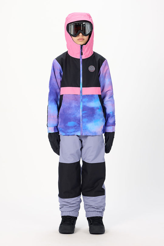 A child modeling a color-blocked winter ski suit with a pink hood, black and purple chest, blue and purple watercolor patterned front, light purple pants, black gloves, and black boots, set against a plain white studio background.