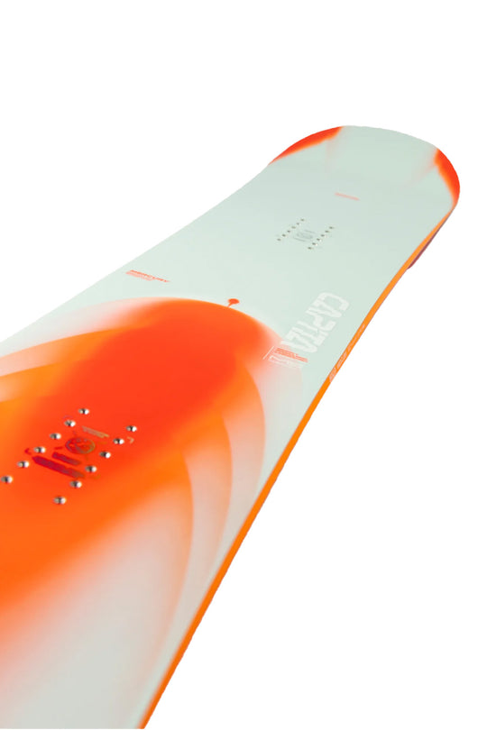 A close-up of a snowboard showing the top sheet, featuring a white base with a vibrant orange graphic and orange binding posts.