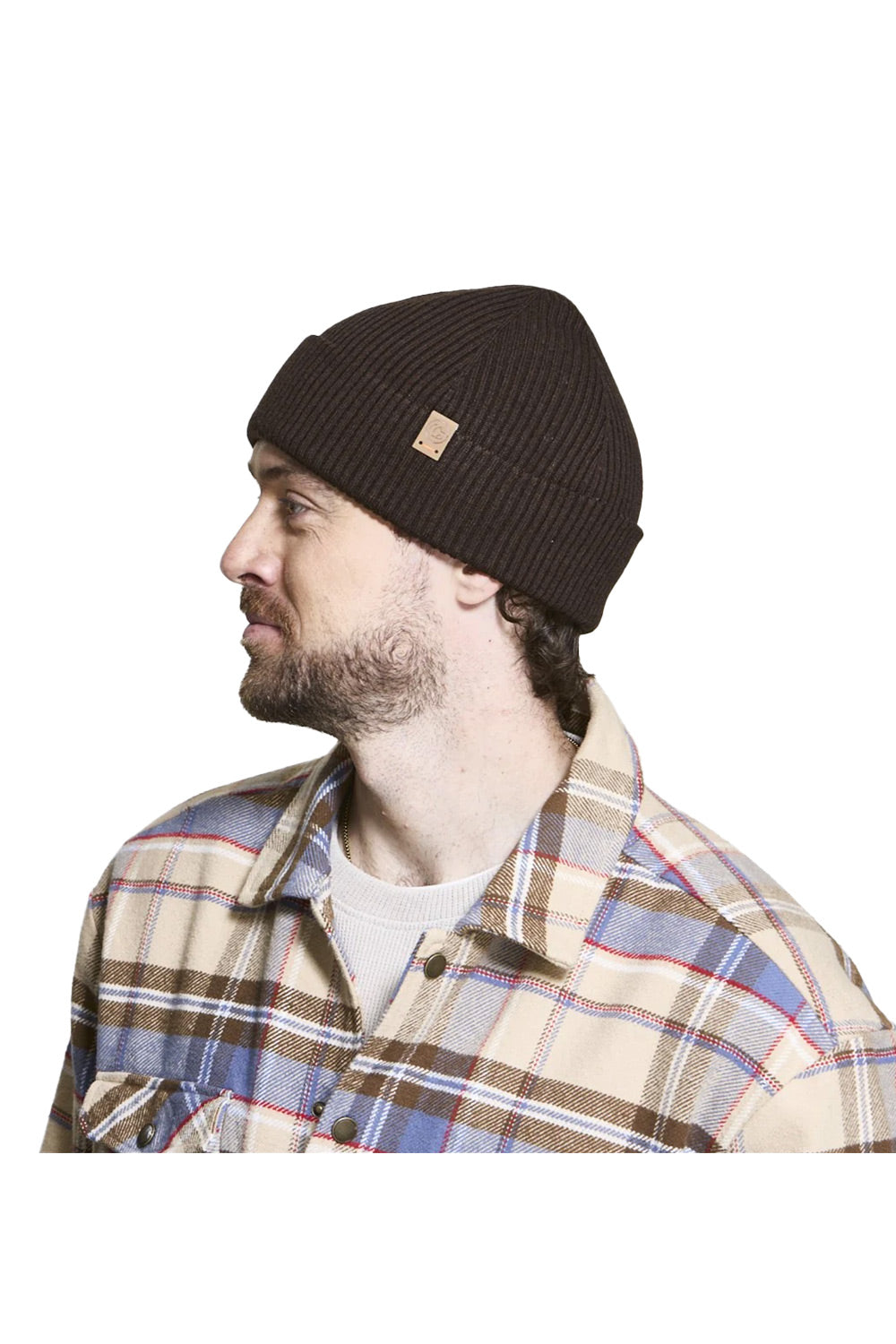 A man in profile wearing a dark brown ribbed knit beanie with a small tan brand patch and a beige plaid button-up shirt, photographed against a plain white background.