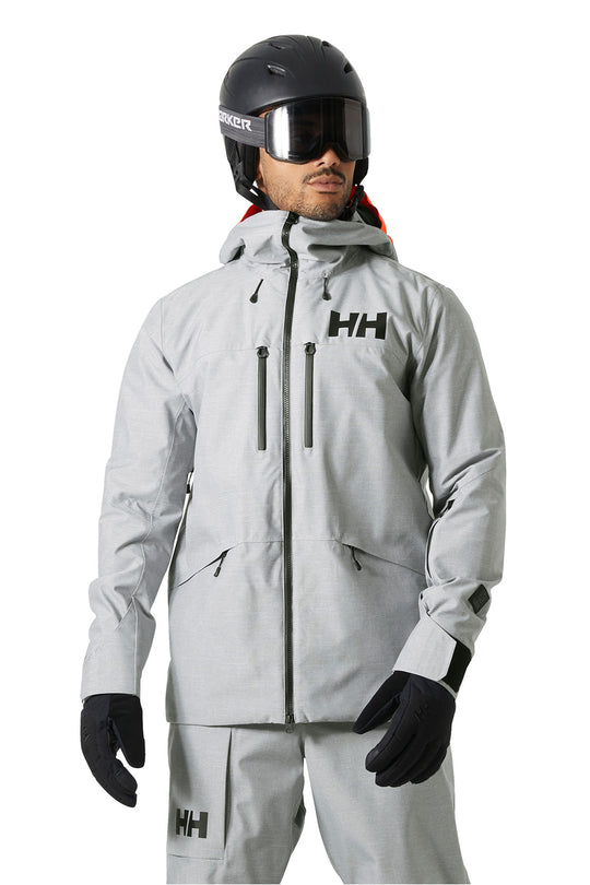 A man wearing a light gray Helly Hansen ski jacket, matching ski pants, black gloves, and a black helmet with goggles, shown against a plain white background.