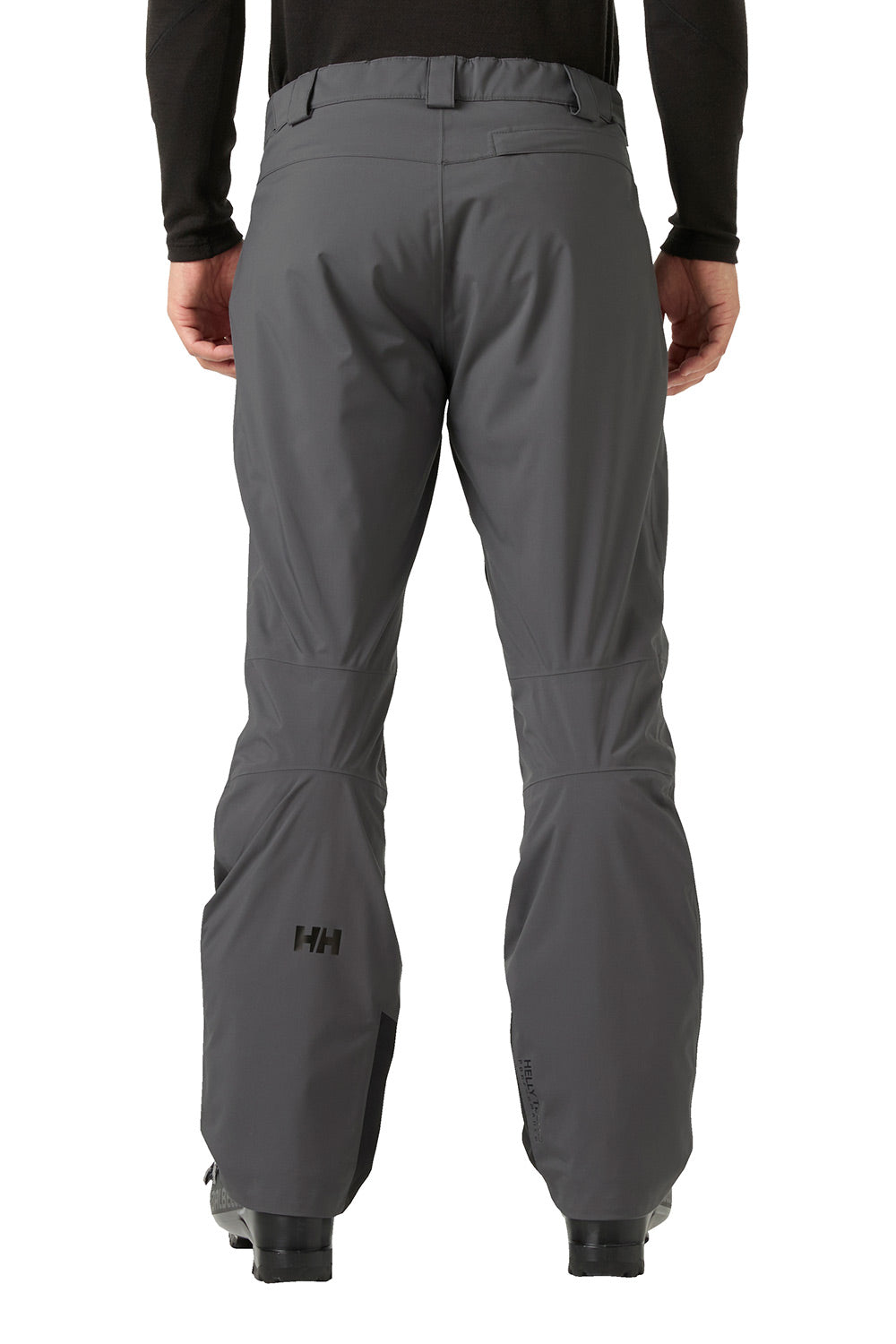 Rear view of a person wearing dark gray technical pants with a black long-sleeve top, shown against a plain white background. A small Helly Hansen 'HH' logo is visible near the lower left leg.