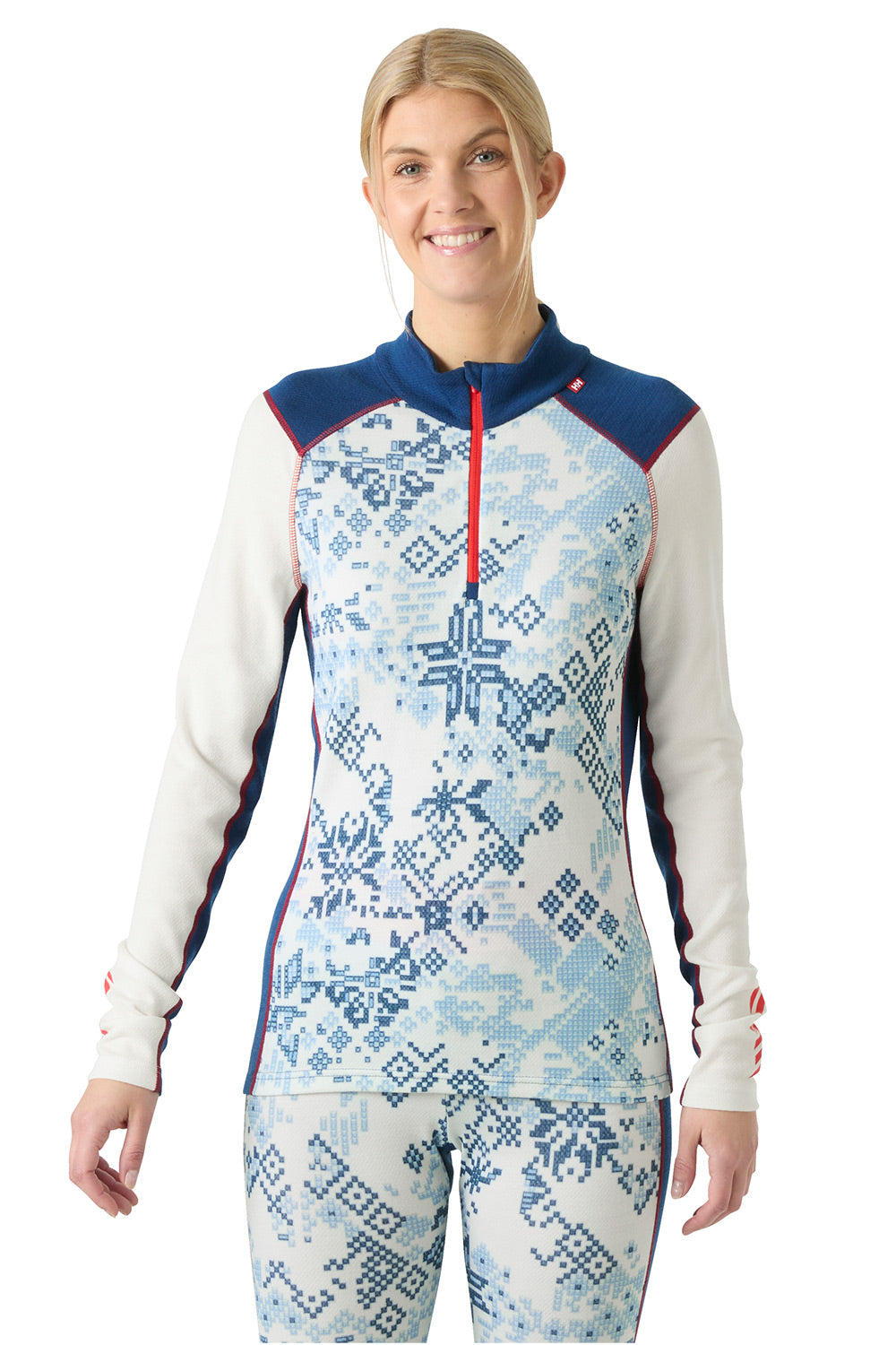 A woman modeling a one-piece athletic top and matching leggings set. The long-sleeve top features a white base with a blue Nordic snowflake pattern, navy blue shoulder yokes, and a red zipper.