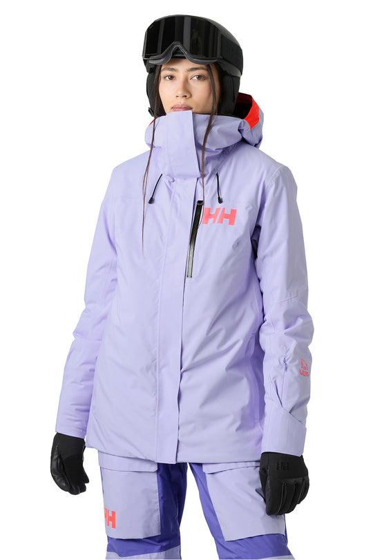 A model wearing a light purple Helly Hansen ski jacket and matching pants, with black gloves, a black helmet, and goggles, against a plain white background.